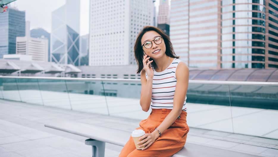 Positive female tourist with caffeine beverage taking rest at urban setting receiving smartphone cell call from friend for talking and communicating, concept of modern technology and generation z