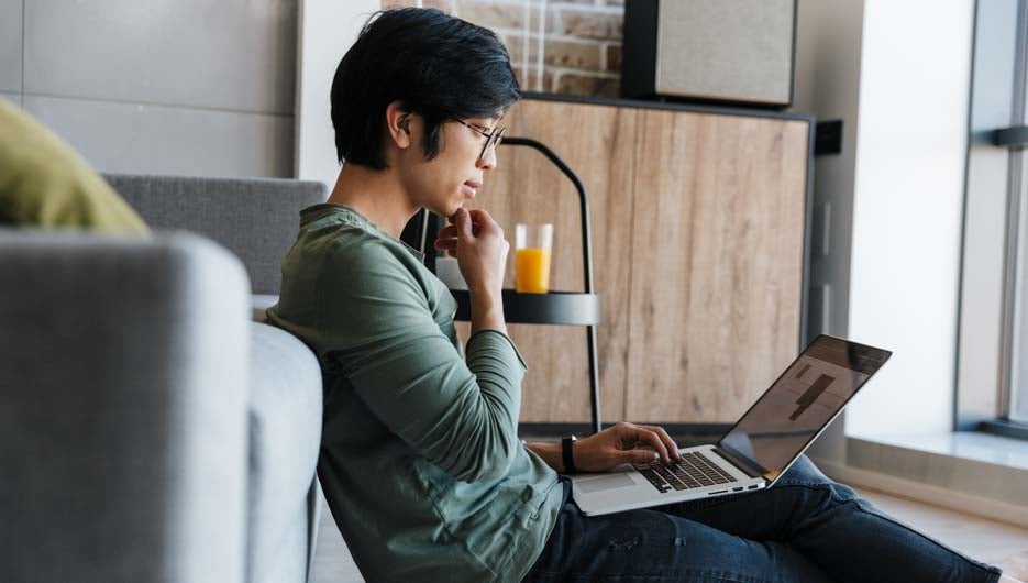 Image of focused asian man working with laptop while sitting