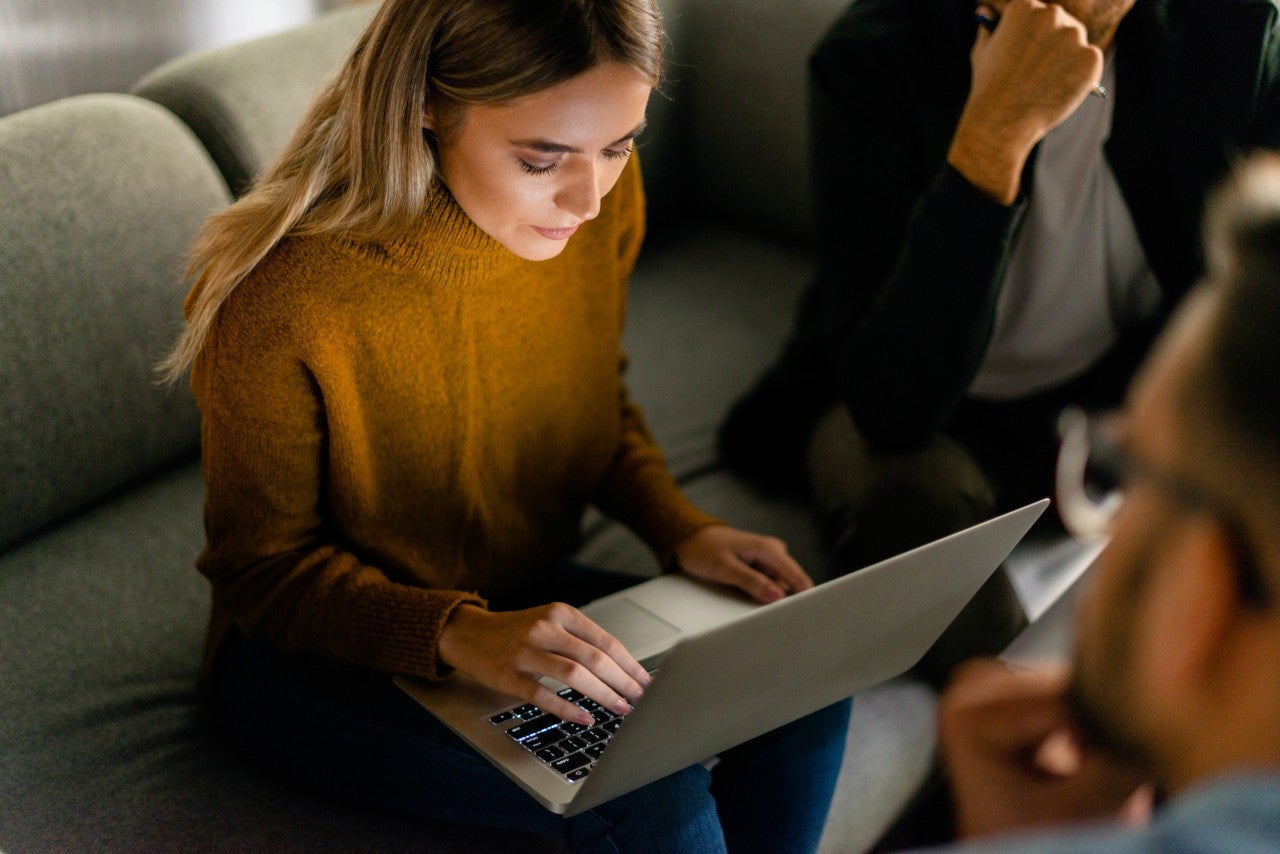 Image of a woman sitting on a sofa and working on her laptop