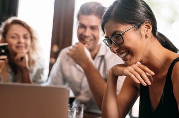 Close up shot of smiling asian woman looking at laptop with friends in cafe. Friends in coffee shop looking at laptop and smiling.